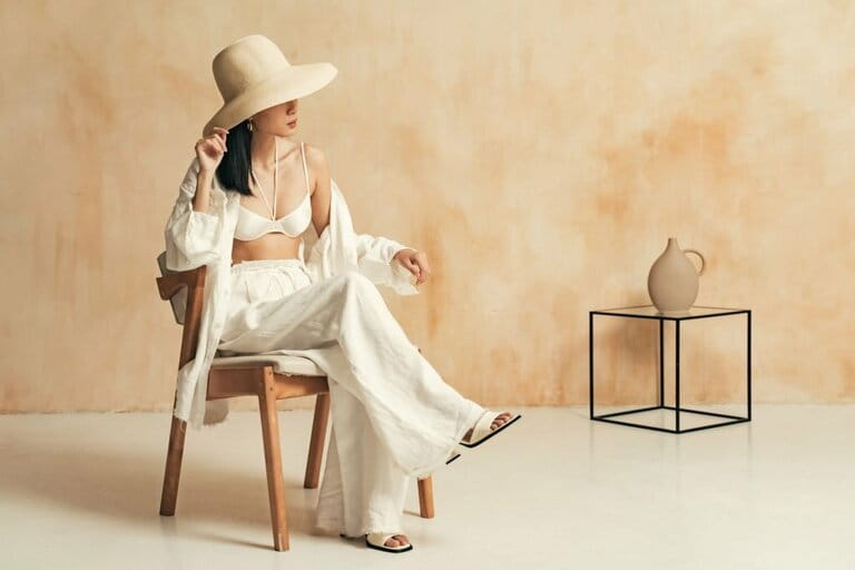 Unrecognizable Asian women in big hats and beach suits sit on chairs in minimalist decor