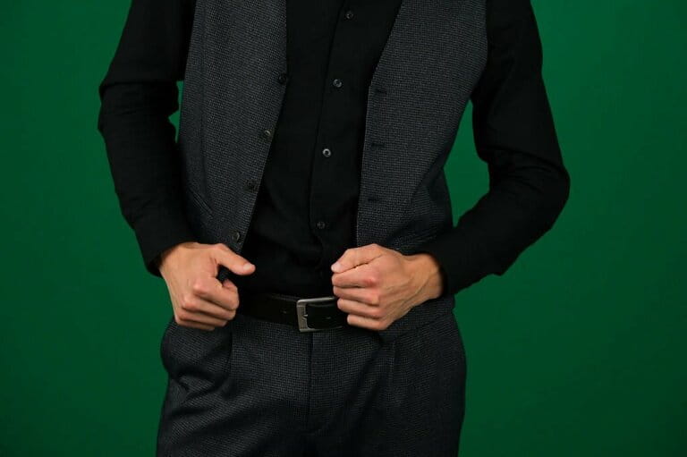 Unrecognizable people give men a vest from a classic three-piece suit, a belt, a black shirt, dark gray clothes on a green background, chromakey tailors, tailors Unrecognizable people give men a vest from a classic three-piece suit, a belt, a black shirt, dark gray clothes on a green background, chromakey tailors, tailors