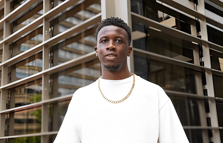 African american male in white t shirt standing on street near building with glass walls and looking at camera