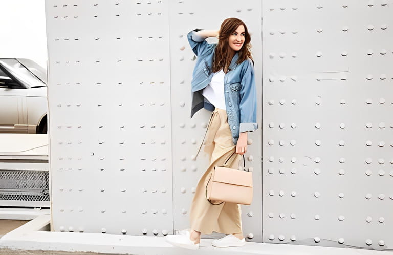 Outdoors fashion portrait of trendy pretty girl posing on the white wall background. Smiling and walking on the city. Going shopping. Wearing stylish wide jean jacket, beige slacks. Outdoors fashion portrait of trendy pretty girl posing on the white wall background. Smiling and walking on the city. Going shopping. Wearing stylish wide jean jacket, beige slacks.