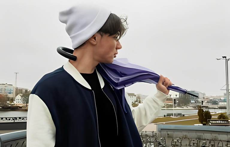 A teenager in a white knit beanie and blue bomber jacket holding an umbrella on a gloomy, rainy day. Street photo.