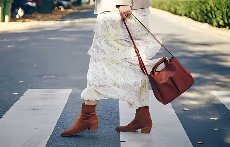 fashion blogger street style. fashionable woman posing wearing an oversized blazer, floral vintage dress, suede cowboy ankle boots and a black trendy mini handbag.