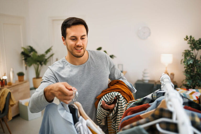 Handsome young man wearing clothes on fabric rack at apartment