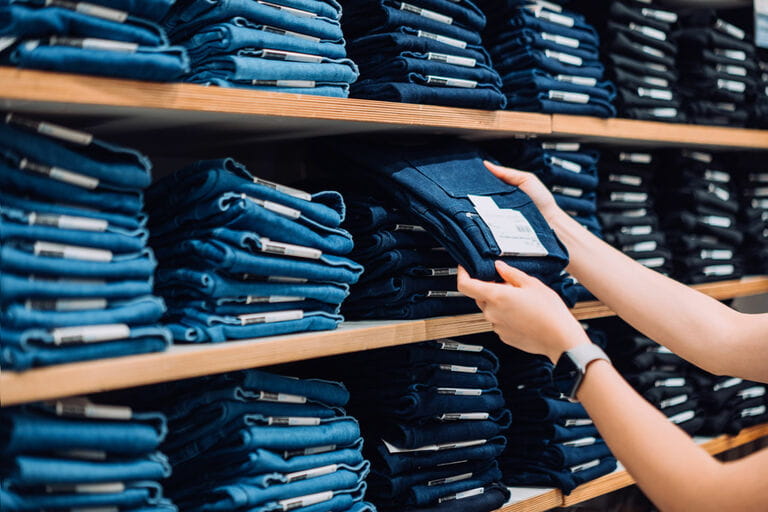 Cropped shot of woman's hand selecting a pair of trousers from the display shelf while shopping in a clothing store in the city Cropped shot of woman's hand selecting a pair of trousers from the display shelf while shopping in a clothing store in the city