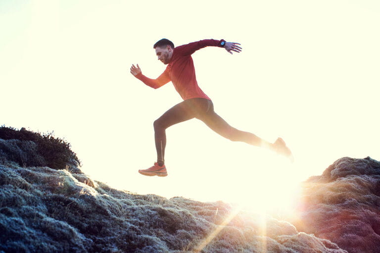 Male runner leaps through sunlit grassy landscape Male runner leaps through sunlit grassy landscape