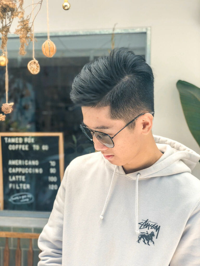 October 3, 2018: Young Asian man with black pompadour hair wearing sunglasses looking down wearing a gray hoodie in front of a restaurant A mature man October 3, 2018: Young Asian man with black pompadour hair wearing sunglasses looking down wearing a gray hoodie in front of a restaurant A mature man