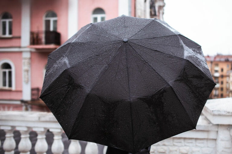Anonymous person standing from behind with large black umbrella on old style buildings