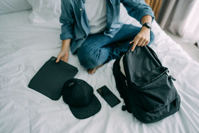 Hipster Asian man packs his rucksack (backpack) in his bedroom in preparation to go away