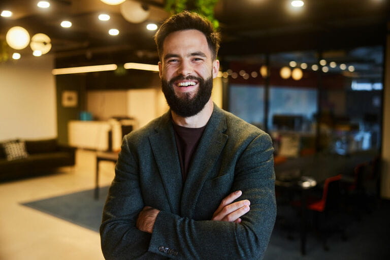 Laughing young businessman standing with arms crossed in office living room Laughing young businessman standing with arms crossed in office living room